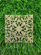 Gold filigree square metal embellishment with ornate scrollwork design on green grass background