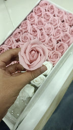 Hand holding a white artificial scented rose beside a box of cream and white soap foam roses