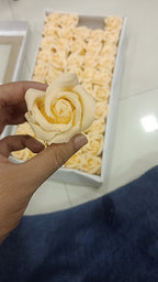 Hand holding a single pink artificial scented rose from a box of pink soap foam roses