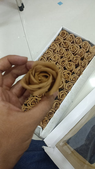 Hand holding a white artificial scented rose beside a box of cream and white soap foam roses