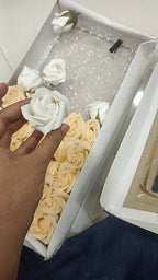 Hand holding a white artificial scented rose beside a box of cream and white soap foam roses